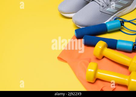 Sneakers, corda da salto, manubri e mini-band per sport e fitness su sfondo giallo con spazio copia Foto Stock