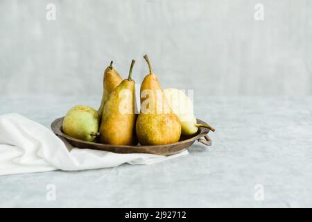 Più pere disposte in una ciotola d'argento su sfondo grigio Foto Stock