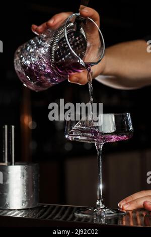 Barista che versa Aviazione, bere con gin, succo di limone, maraschino liquore e crema di liquore viola in un bicchiere. Foto Stock