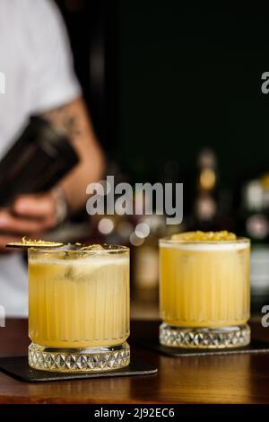 Cocktail dai colori caldi. Cocktail mezcal e cocktail alcolico Scotch Whiskey Penicillin drink. Bicchiere da cocktail sul banco del bar. Foto Stock