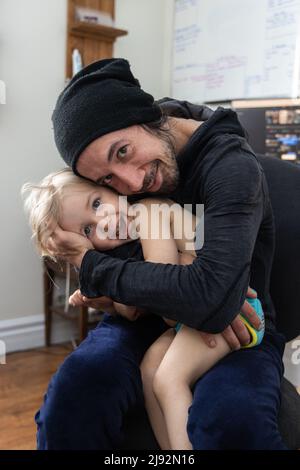 Felice ritratto di padre di trent'anni con figlio di tre anni. Papà cuddles sorridente bambino sano a casa. Momento di famiglia heartwarmming. Foto Stock