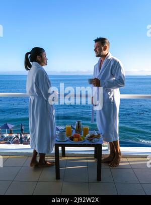 Città del Capo Sud Africa coppia uomo e donne bere caffè durante sul balcone alba in vacanza a Città del Capo Sud Africa. Uomini europei e donne asiatiche si svegliano con il caffè che si affaccia sull'oceano Foto Stock