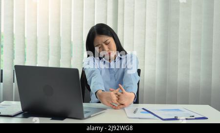 Donna asiatica che si siede per molto tempo e si prende dolore e allunga i suoi muscoli. Foto Stock