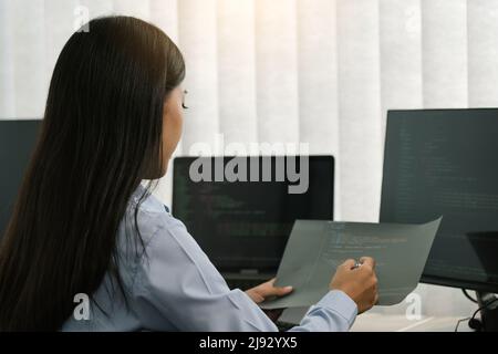 Donna asiatica sviluppatori di software seduti di fronte ai computer guardando i codici computer sullo schermo. Foto Stock