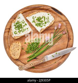 fette di pane a grani interi con formaggio cremoso, erba cipollina tritata verde, pepe e sale su un tagliere di legno isolato su bianco Foto Stock