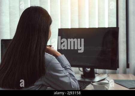 Donna asiatica sviluppatori di software seduti di fronte ai computer guardando i codici computer sullo schermo. Foto Stock