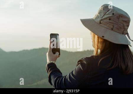 Le donne asiatiche usano i loro telefoni cellulari per scattare foto del paesaggio in cima a una fresca collina di montagna. Foto Stock