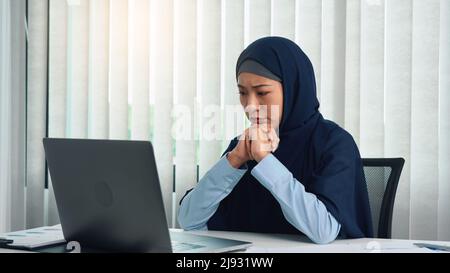 La donna musulmana guarda lo schermo di un computer e viene sollecitata. Foto Stock