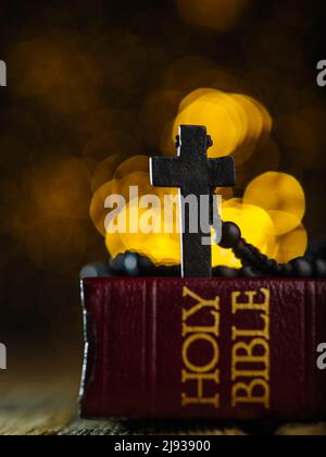 Su uno sfondo giallo con luci sfarfallate, c'è un libro rosso - la Sacra Bibbia e una croce cattolica nera sul rosario. Minimalismo. Non ci sono Foto Stock