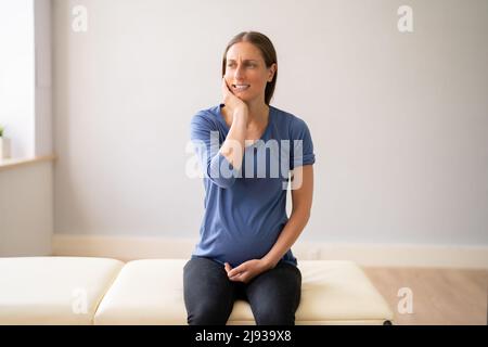 Giovane donna incinta con espressione dolorosa che soffrono di mal di denti in clinica Foto Stock