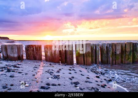 groynes che si aggirano nel mare al tramonto. Spiaggia con pietre in primo piano. Preso a zingst sul darss. La prospettiva è diretta all'orizzonte Foto Stock