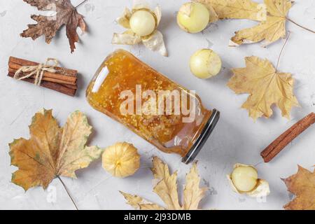 Marmellata di physalis trasparente fatta in casa con cannella in vaso di vetro su sfondo grigio chiaro, vista dall'alto Foto Stock