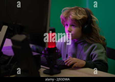 Bambini che usano il pc di notte. Bambino con computer in una stanza buia. Un bambino piccolo usa una scrivania di notte, un bambino con lo schermo del computer in camera. Foto Stock