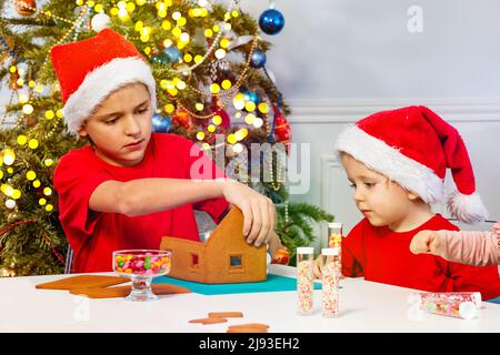Due bambini decorano la casa di pan di zenzero insieme in cappelli di Santa Foto Stock