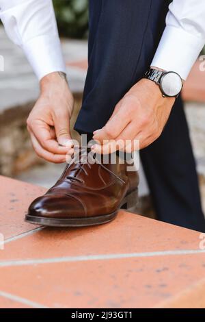 Un uomo d'affari o uno sposo è vestito con scarpe classiche ed eleganti in uno spazio all'aperto. Primo piano mani e scarpe. Primo piano vista di maschio mani allacciamento beautiff Foto Stock