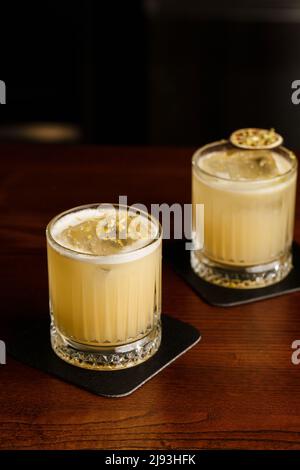 Cocktail dai colori caldi. Cocktail mezcal e cocktail alcolico Scotch Whiskey Penicillin drink. Bicchiere da cocktail sul banco del bar. Foto Stock