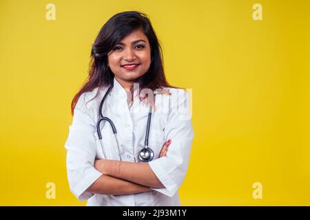 Donna indiana giovane e bella donna bionda medico ginecologo utilizzando stetoscopio in un cappotto medico bianco su sfondo giallo in studio Foto Stock