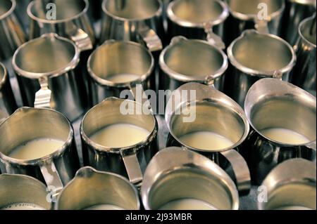 Un raggruppamento di piccoli contenitori di latte in metallo da letto dell'ospedale, tutti contenenti latte. Foto Stock