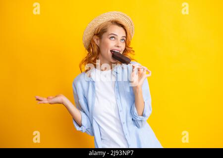 Ritratto di ragazza rossa con gelato al cioccolato su sfondo giallo. Donna curly allegra che mangia gelato. Foto Stock