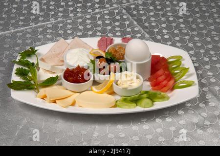 Un piatto da colazione con marmellata, formaggio, pomodori, peperoni, cetrioli, olio, miele, uova, salumi e salsicce. Foto Stock