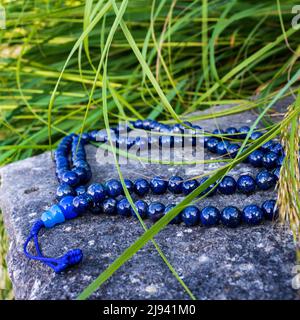 Perle di preghiera buddista blu per il mantra mediaon, primo piano sulla roccia con erba verde in natura. Accessorio spirituale Foto Stock