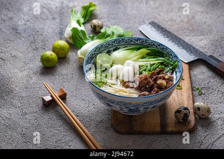 Zuppa di ramen giapponese con pollo, uova, erba cipollina e bok su sfondo di cemento. Foto Stock