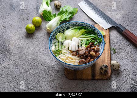 Zuppa di ramen giapponese con pollo, uova, erba cipollina e bok su sfondo di cemento. Foto Stock