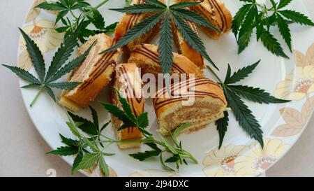 Rotolo dolce con olio di marijuana su piatto bianco. Cucina di cannabis. Disposizione dei deliziosi dessert, vista dall'alto da vicino. Foto Stock