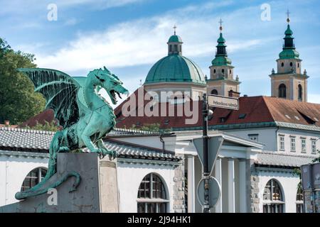 Ljubljana, Slovenia - 07.15.2021: Scultura in bronzo del drago con il cielo blu e la cattedrale sullo sfondo, guardando a destra Foto Stock