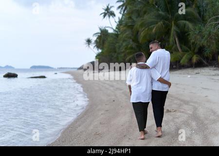 Coppia gay che cammina lungo una spiaggia la sera Foto Stock