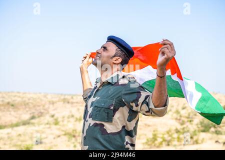 Vista laterale scatto di felice esercito indiano soldato che tiene ondeggiante bandiera indiana in cima a mountian - concetto di orgoglio nazionale, nazionalismo, libertà e. Foto Stock