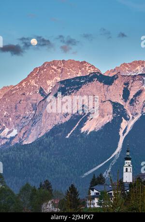 La luna piena sorge sulle ripide vette della catena montuosa di Wetterstein, sopra Ehrwald in Tirolo Austria, Landscape Foto Stock