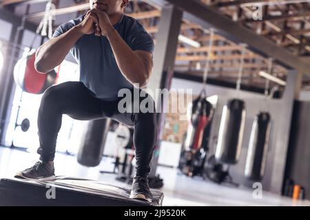 Sezione bassa del giovane pugile maschile afroamericano che squatting sulla scatola nera di esercizio al centro benessere Foto Stock