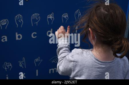 Una giovane ragazza guarda un grafico di linguaggio dei segni in un parco giochi a Edmonton, Alberta, Canada Foto Stock