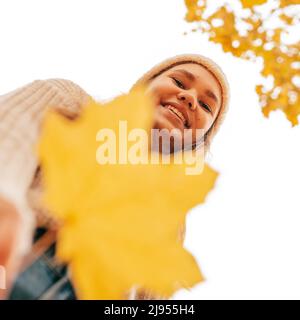 Giovane donna ridente in maglia guarda il fotografo dall'alto, si è rivelata sullo sfondo del cielo luminoso. Tiene la grande foglia gialla dentro Foto Stock