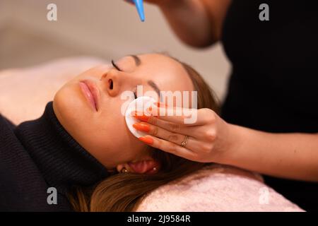 Mani di specialista di bellezza strofinando il cotone sul volto del cliente femminile Foto Stock