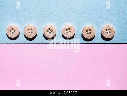 Composizione di bottoni per cucire identici monocromatici su sfondo rosa e blu. Disposizione piatta, layout e piano portapaziente con spazio di copia. Foto Stock