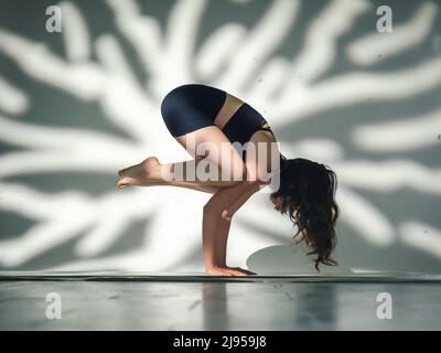 Una giovane donna cacucasiana, che esercita lo yoga. Girato in studio con patterin astratto di luce dietro sullo sfondo. Foto Stock