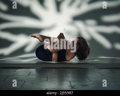 Una giovane donna cacucasiana, che esercita lo yoga. Girato in studio con patterin astratto di luce dietro sullo sfondo. Foto Stock