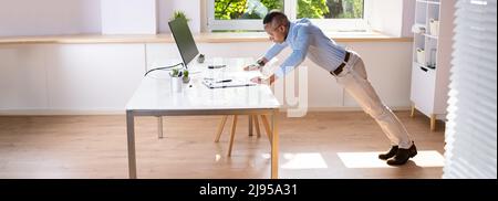 Vista laterale DI un giovane uomo d'affari che fa la spinta in su sulla scrivania dell'ufficio Foto Stock