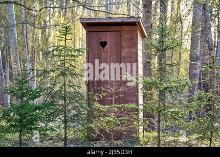 servizi igienici esterni in legno con cuore sulla porta. Alberi di abete rosso intorno. Foto Stock