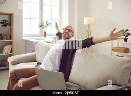 L'uomo adulto felice che ha finito il suo lavoro sul portatile è seduto sul divano e rilassante Foto Stock