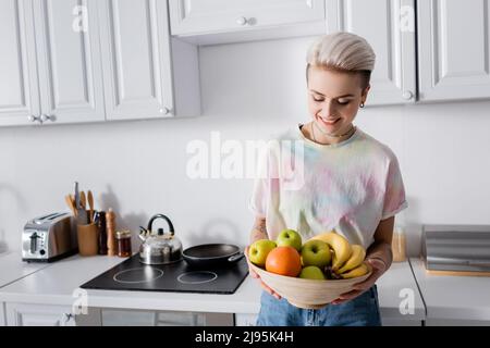 donna allegra con ciotola trendy di pappe di frutta matura in cucina Foto Stock