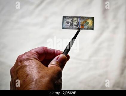 Mano della donna con una pinza che tiene una piccola banconota da cento dollari USA, con sfondo chiaro Foto Stock