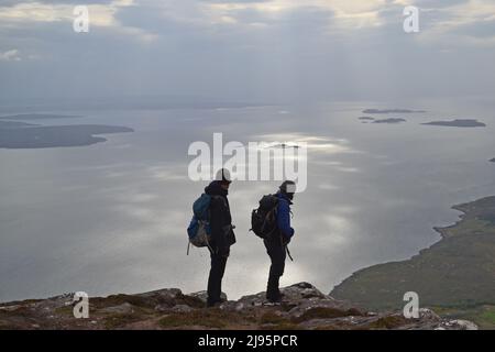 Escursionisti/escursionisti in collina con silhouette su ben Mor Coigach, una cresta vicino Ullapool, Scozia nord-occidentale, Assynt, ammirare le viste delle isole estive in una giornata di primavera Foto Stock