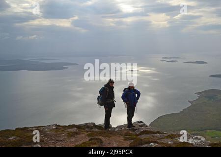 Escursionisti/escursionisti in collina con silhouette su ben Mor Coigach, una cresta vicino Ullapool, Scozia nord-occidentale, Assynt, ammirare le viste delle isole estive in una giornata di primavera Foto Stock