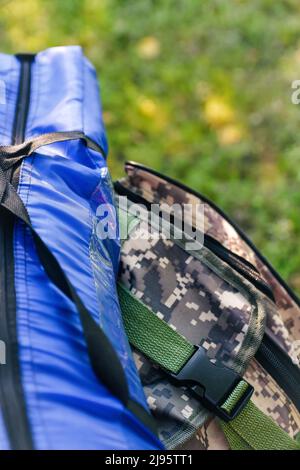 Zaino militare defocus e tenda blu o sacco a pelo. Borsa esercito su sfondo verde erba vicino albero. Zaino militare mimetizzazione. Turismo summ Foto Stock