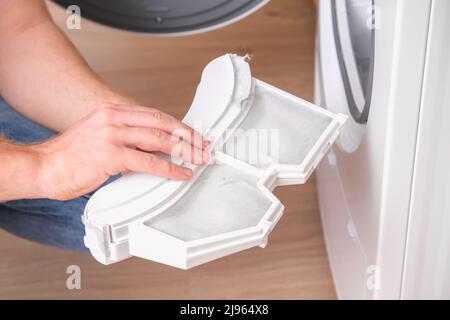 Un uomo prende un filtro di pelucchi fuori dall'asciugatore e lo pulisce da polvere, lanugine, capelli, lana. Foto Stock