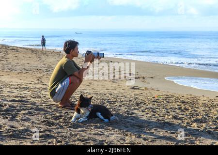 Un fotografo locale accovacciato sulla sabbia e che scatta foto ai surfisti a Batu Bolong Beach, Canggu, Bali, Indonesia Foto Stock
