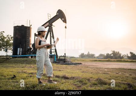 Ingegneria petrolchimica asiatica donna con casco di sicurezza in piedi nella struttura petrolifera industria petrolchimica. Foto Stock